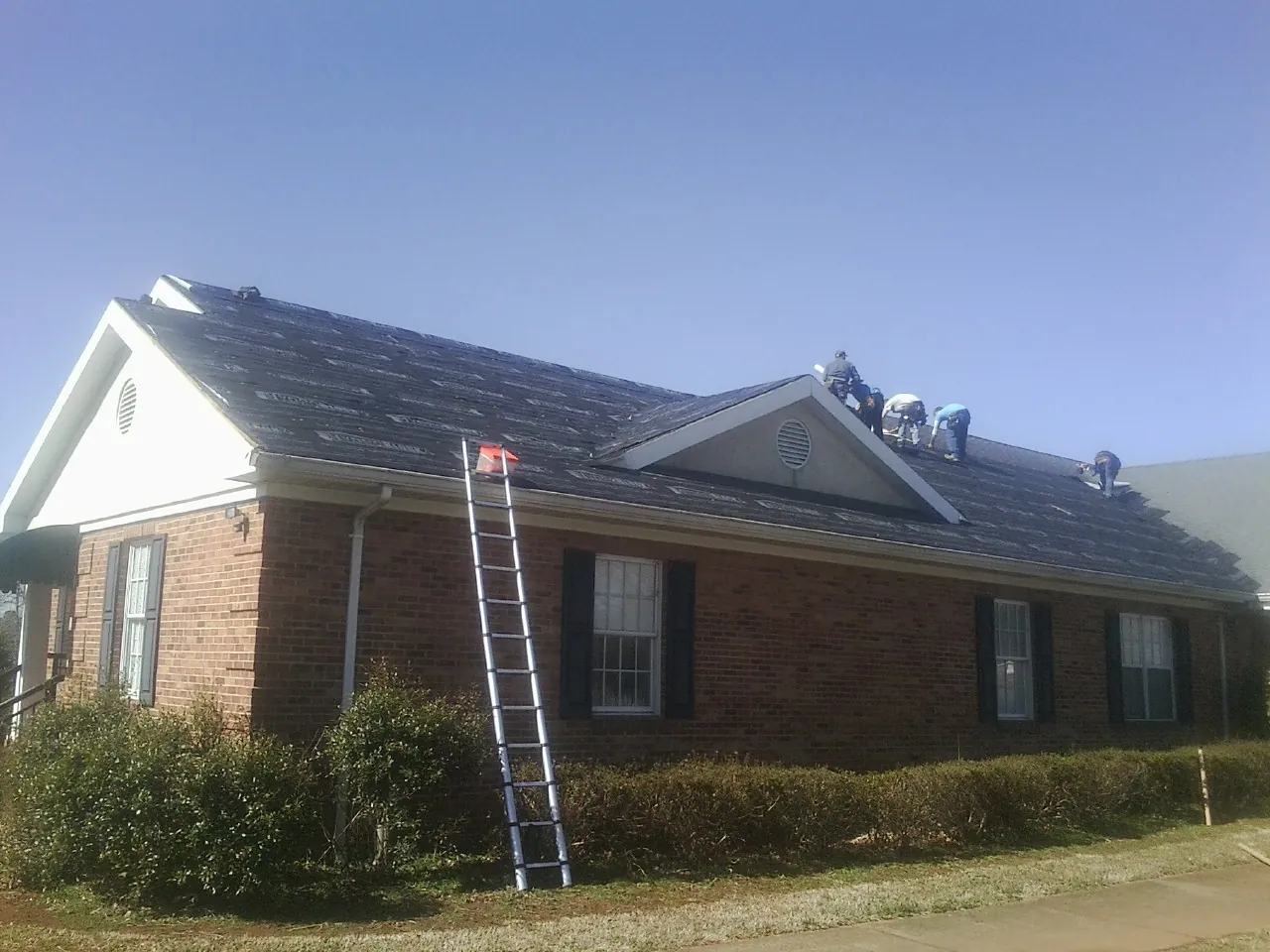 Crew tearing shingles off a brick ranch roof with a ladder set — Emergency Roof Repair work by our crew in Fort Wayne