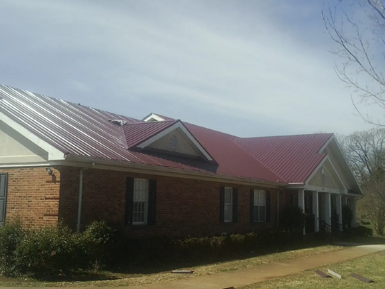 Red metal roof with gabled entries on a long brick building, from a Hail Damage Roof Repair job in Fort Wayne