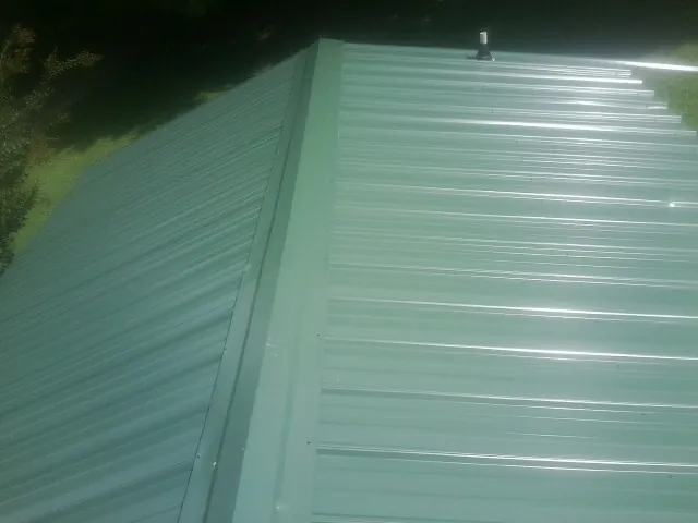 New green metal panels meeting at the ridge of a roof — Flat Roof Repair work by our crew in Fort Wayne