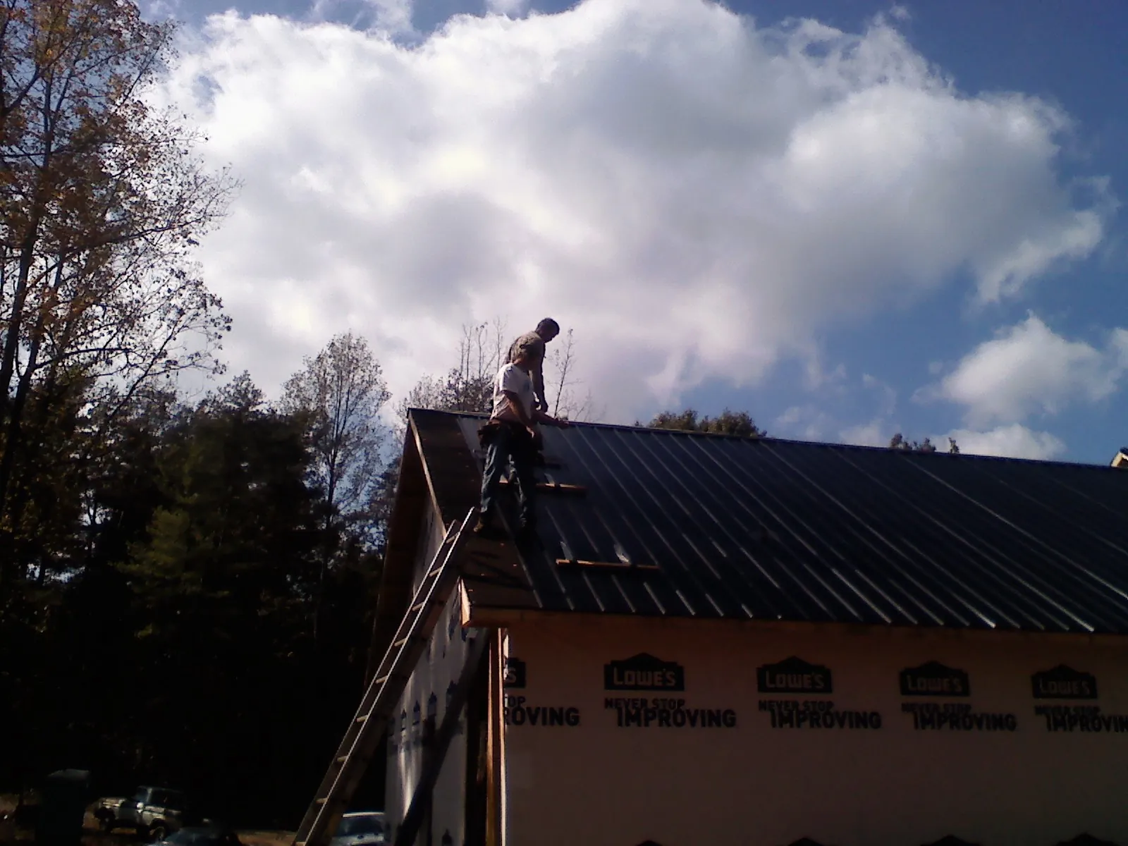 Roofer fastening dark metal panels high against a cloudy sky, from a Roof Inspection job in Fort Wayne
