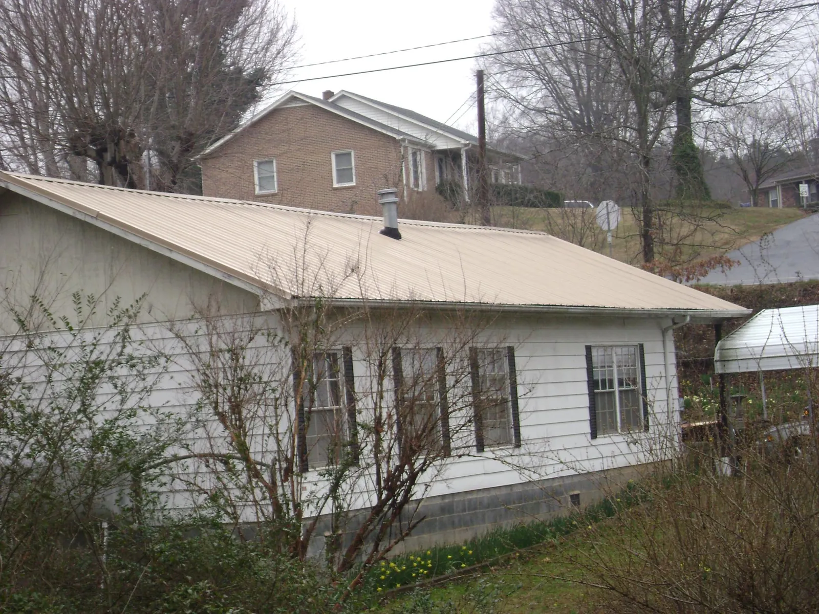 Tan metal roof on a white sided house set into a hillside — Commercial Roofing by Roofing Brothers in Fort Wayne